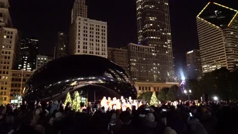 Menschen-Hören-Weihnachtslieder-Und-Feiern-Winterferien-In-Der-Nähe-Von-Cloud-Gate-In-Der-Innenstadt-Von-Chicago-Mit-Einem-Wolkenkratzer-Im-Hintergrund