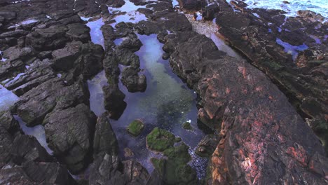 Drohne-Fliegt-über-Felsige-Küste-Mit-Spiegelung-Des-Blauen-Himmels-Bei-Bahia-Bustamante