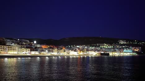 Portugal,-Sesimbra-Bei-Nacht-Vom-Meer-Aus,-Während-Sich-Die-Lichter-Der-Stadt-Auf-Dem-Atlantischen-Ozean-Spiegeln