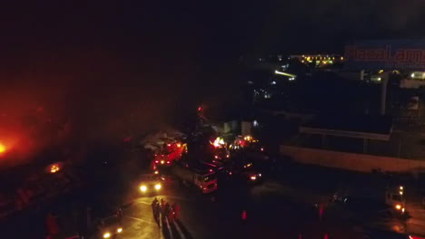 Aerial,-tilt-up,-drone-shot-overlooking-firetrucks-and-firemen-extinguishing-a-building-on-fire,-during-night-time,-in-Dominican-republic