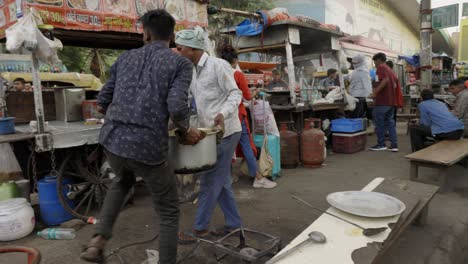 Men-lifting-pot-with-food-into-street-shop,-Delhi-India
