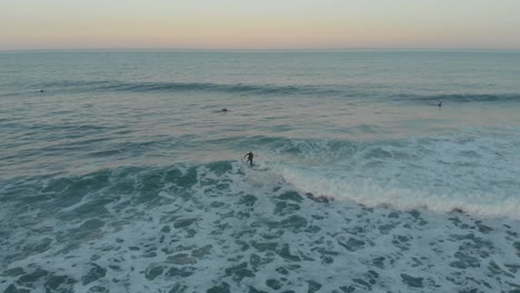 Surfer-balancing-on-the-mild-foamy-waves-of-beach-Santinho-at-golden-hour-time