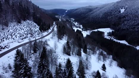 Aerial-low-fly-view-of-mountain-road-with-snow-capped-forests-during-winter-in-Hautes-Vosges,-France
