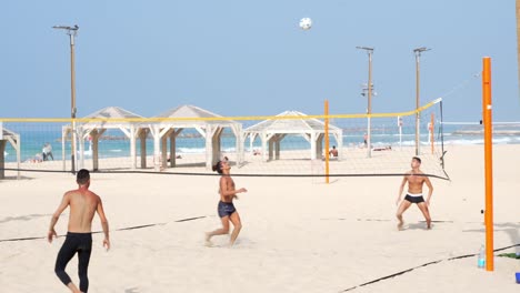 Four-young-people-men-playing-beach-volley-together-by-the-sea-on-a-sunny-summer-vacation-day