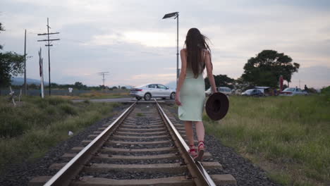 Model-in-summer-dress-playfully-balancing-on-train-track-rail---Backview-Tracking-shot