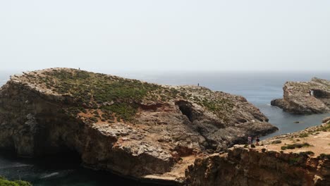 Tourists-Walking-On-Small-Islet-By-Crystal-Lagoon,-In-Comino-Island