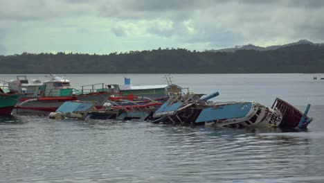 Kleine-Boote-Liegen-Im-Hafen-Der-Stadt-Surigao-Inmitten-Der-Ruinen-Von-Booten,-Die-In-Taifunen-Gesunken-Sind