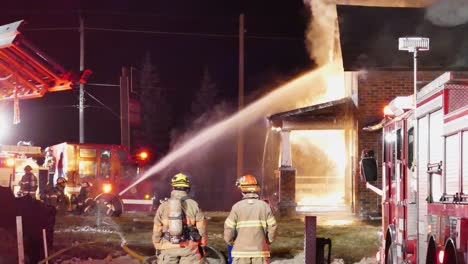 Fire-fighters-connect-hose-and-spray-up-towards-front-of-house-to-extinguish-fire-at-night