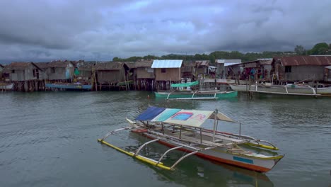 Small-Banka-boats-float-in-front-of-the-floating-slums-of-Surigao-City,-Mindanao,-Philippines