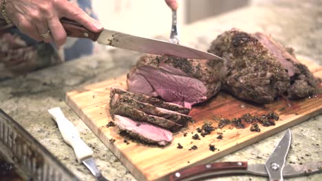 In-a-bright-kitchen-on-Christmas,-a-woman-joyfully-carves-succulent-roasted-lamb-on-a-bamboo-cutting-board,-capturing-the-warmth-of-festive-tradition