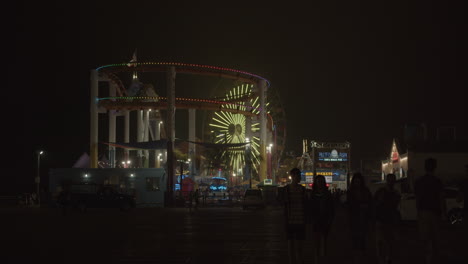 An-exterior-shot-of-the-amusement-park-on-Santa-Monica-Pier-at-night-in-slow-motion-with-tourists-walking-by-and-famous-Pacific-Park-ferris-wheel-in-background