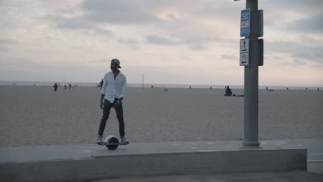 Slow-motion-shot-of-man-riding-electronic-skateboard-with-beach-in-the-background-during-sunset-in-Santa-Monica,-CA