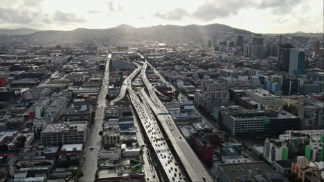 Aerial-of-San-Francisco-cityscape,-highway-traffic-under-the-cloudy-grey-sky,-California,-USA