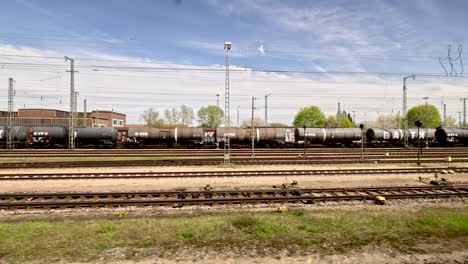 Looking-Out-Window-Of-Moving-Train-Passing-Through-Railyard-Past-Freight-Trains-In-Germany-On-Public-Transport