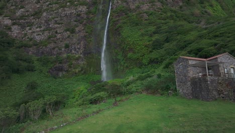 Flying-towards-cascata-do-poço-do-bacalhau-waterfall-with-house-at-Flores-island---Drone-shot