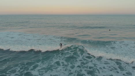 Surfer-cruising-the-calm-mild-waves-of-the-beach-of-Santinho-at-golden-hour-evening
