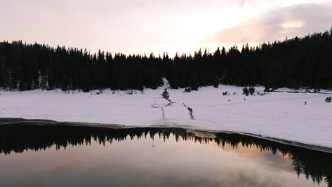 Reverse-aerial-reveals-winter-sunrise-and-forest-reflection-in-clear-alpine-lake