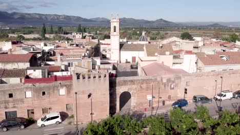 Langsamer-Vorbeiflug-In-Einem-Hohen-Winkel-über-Dem-Mittelalterlichen,-Von-Mauern-Umgebenen-Dorf-Mascarell-Und-Seinen-Dächern-Und-Seinem-Glockenturm-In-Spanien