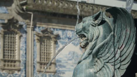 Close-Up-Shot,-Green-Winged-Lion-fountain-in-Porto,-Church-Igreja-do-Carmo-in-the-background