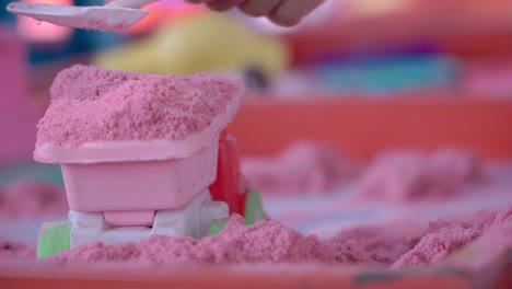 Child's-hands-are-playing-with-pink-sand-using-a-toy-shovel