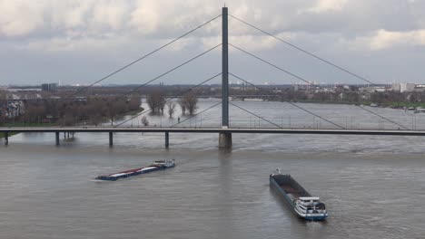 Barcazas-Por-El-Puente-Oberkasseler-Dusseldorf-Durante-La-Inundación-Navideña-Del-Río-Rin-En-2023,-Nivel-Del-Agua-770-Cm