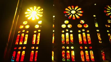 Tilting-UpShot,-Scenic-View-of-Red-and-Yellow-Stained-Designed-Glass-of-Sagrada-Familia-Church,-Sun-Light-Passing-through-the-Glass-in-the-background