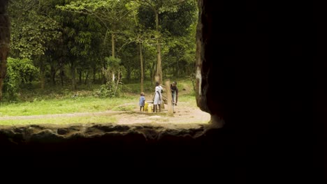 Tres-Niños-Van-A-Buscar-Agua-A-Una-Fuente-Con-Contenedores-Amarillos-Y-Un-Bosque-Al-Fondo,-Cerca-De-Entebbe,-Uganda