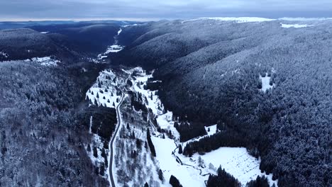Aerial-view-of-mountain-road-with-snow-capped-forests-and-valley-during-winter-in-Hautes-Vosges,-France