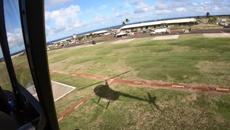 Helikopter-Mit-Offener-Tür-Landet-Auf-Einem-Kleinen-Flughafen-In-Hawaii,-Mit-Schattensilhouette-Von-Propellern