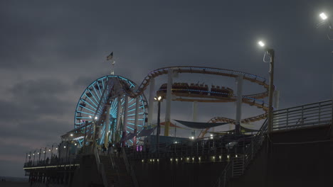 A-slow-motion-shot-of-Pacific-Park-in-Santa-Monica,-CA-during-the-night-in-summer-with-rollercoaster-and-ferris-wheel-in-background