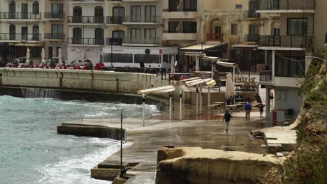 Waves-Crashing-On-The-Port-Where-People-Walking,-In-Marsalforn