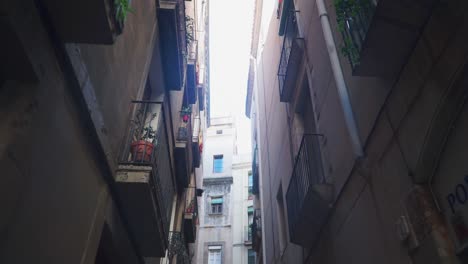 Nach-Oben-Neigende-Aufnahme,-Malerischer-Blick-Auf-Eine-Enge-Straße-In-Barcelona,-Einander-Zugewandte-Fenster,-Heller-Himmel-Im-Hintergrund