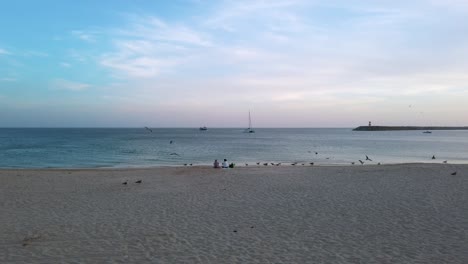 Paar-Sitzt-Am-Sandstrand-Und-Starrt-Auf-Den-Atlantik-Zwischen-Möwen-Nach-Sonnenuntergang-In-Sesimbra,-Portugal