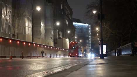 Double-decker-bus-and-cyclist-drive-down-a-rainy-alley-during-rush-hour-at-night-London-UK