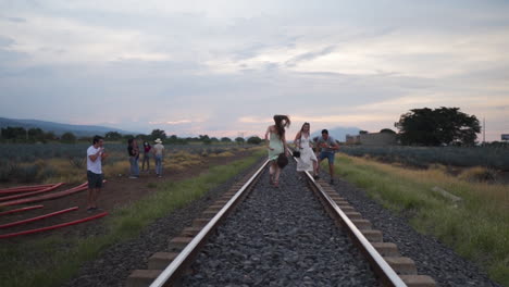 Woman-running-on-railway-among-group-of-people-enjoying-the-sunset---Wide-Follow-shot