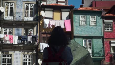 Dolly-Out-Shot,-woman-with-a-red-backpack,-standing-on-her-balcony-on-a-Sunny-day-in-Riberia-Square-in-Porto
