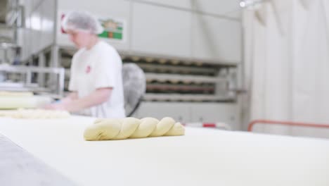 Low-Angle-View-Of-Fresh-Triple-Dough-Baguette-On-Moving-Conveyor-Belt-With-Worker-In-Background