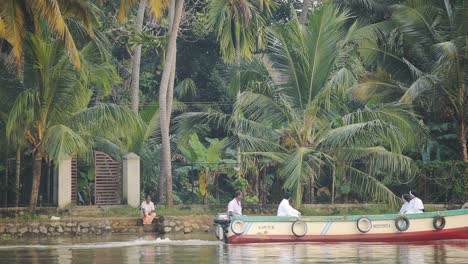Local-men-on-a-traditional-boat-on-a-river-flowing-near-palm-trees,-Kerala-Backwaters,-India
