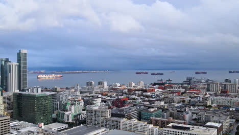 Panoramic-aerial-of-San-Francisco-city-skyline-buildings,-South-Beach-Harbour-Bay-ferry-pier-and-industrial-ships-in-background-under-stormy-sky,-CA,-USA