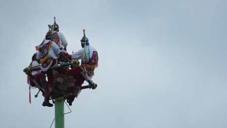 Papantla-dancers-on-the-top-of-the-pole,-playing-drums-during-a-cloudy-day