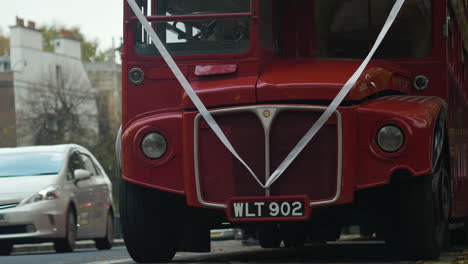 Close-up-shot-front-grill-of-a-retro-double-decker-bus-parked-alongside-a-busy-street