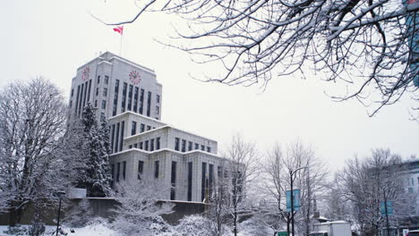 A-RIGHT-TO-LEFT-DOLLY-SHOT-Past-Trees-Towards-a-Snowy-Vancouver-City-Hall-During-a-Cold-Overcast-Day