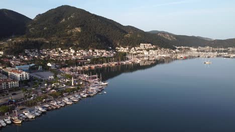 Filmische-Luftaufnahme-Der-Stadt-Fethiye-Mit-Geparkten-Booten-An-Der-Mittelmeerküste-Und-Bergen-Im-Hintergrund,-Türkei