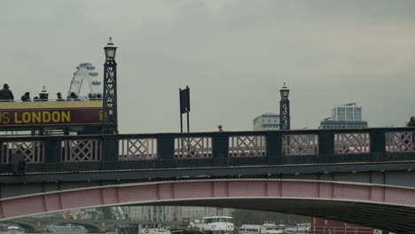 Der-Londoner-Tourbus-überquert-Die-Lambeth-Bridge-An-Einem-Bewölkten-Tag-Mit-Dem-London-Eye-Im-Hintergrund