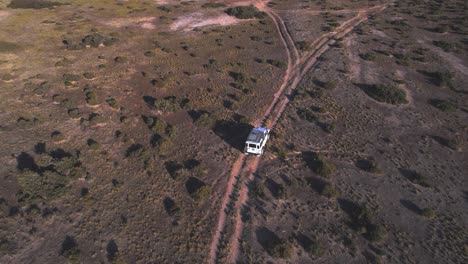 Tilt-Up-Drone-view-revealing-a-Car-driving-on-the-dirt-road-through-the-plains-leading-to-the-beach-at-bahia-bustamante