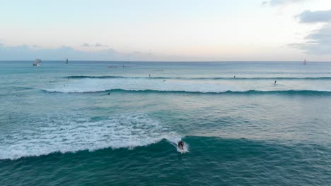 Aerial-Tracking-Shot-of-Girl-Surfing-at-Golden-Hour-on-Waikiki-Beach,-Hawaii