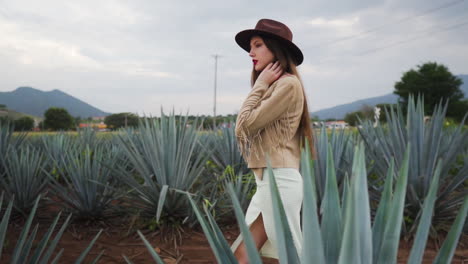 Confident-Young-woman-in-cowboy-hat-and-summer-dress-crossing-Tequila-Pineapple-fields-in-Mexico---Medium-tracking-slow-motion-shot