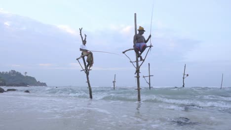 A-Couple-Of-Local-Stilt-Fishermen-Sitting-And-Fishing-On-The-Ocean-In-Weligama,-Matara,-Sri-Lanka