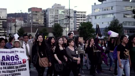 Men-and-women,-mostly-wearing-black,-are-marching-and-holding-signs-during-protest-in-the-International-Women's-Day-in-Quito