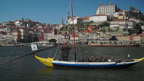 Full-shot,-Traditional-boat-floating-on-the-Douro-River-in-Porto,-Portugal,-Scenic-view-Old-Town-in-the-background